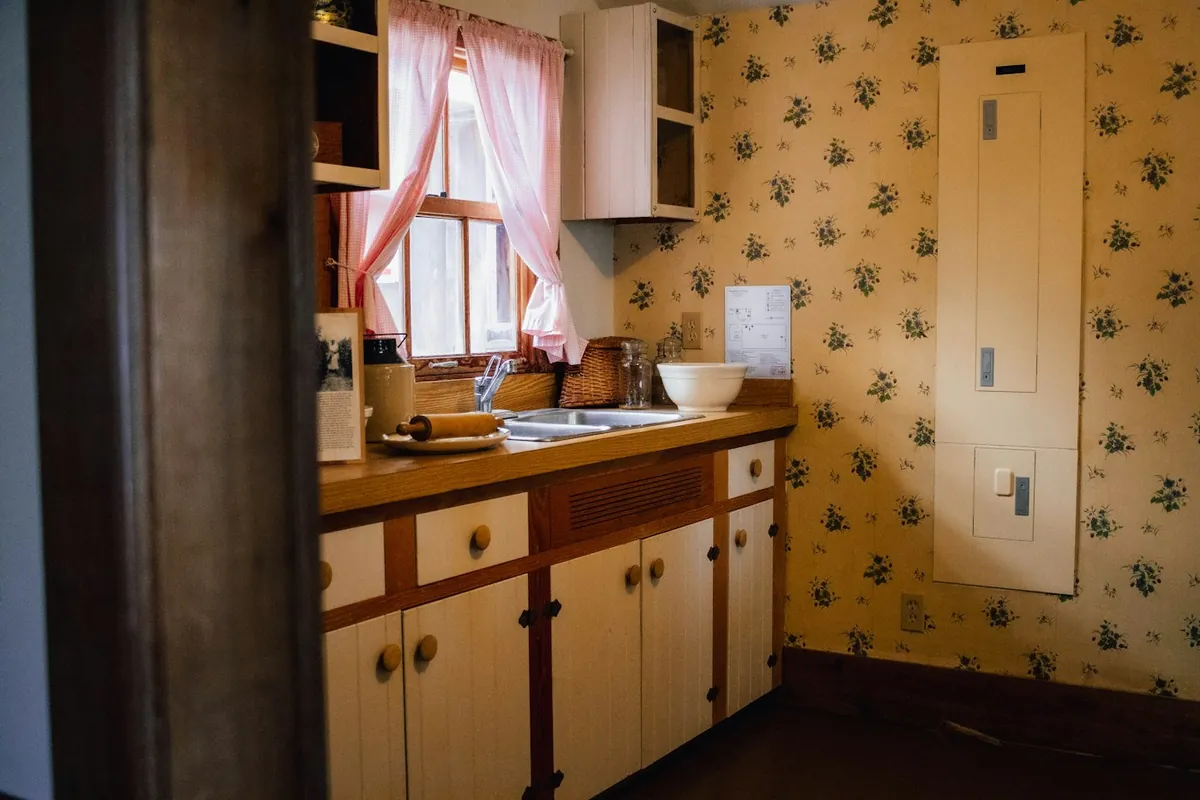 An original mid-century painted kitchen with a wood-edged counter, wallpaper and a fuse panel, the kind of pre-1978 interior the federal lead rules cover