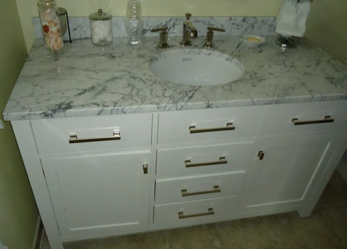 White shaker bathroom vanity with a marble top, undermount basin and brushed brass bar pulls